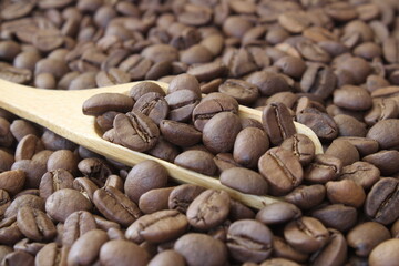 Roasted coffee beans in wooden scoop on brown burlap or sack cloth background.