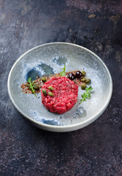 Modern Style Gourmet Tartar roh vom Rinderfilet mit Kapern und Amarena Kirschen serviert mit Tr&uuml;ffelcreme und Salat als close-up in einer Nordic Design Schale