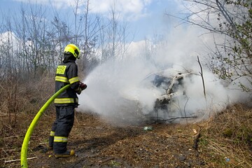 A firefighter extinguishes a fully involved car fire with water from a hose