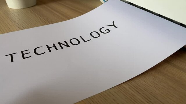 Printing &ldquo;TECHNOLOGY&rdquo; text written message on paper sheet document. Close up A4 page being printed from multifunction scanner printer on wooden desk in office. Hand take paper from printer
