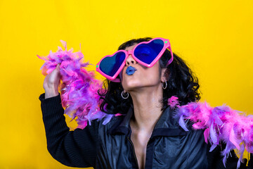 Young woman wears large heart-shaped glasses and a scarf with pink and purple feathers. Beautiful woman sends a kiss. Party concept.