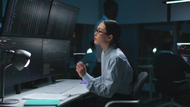 Asian female programmer staring at computer monitors with data
