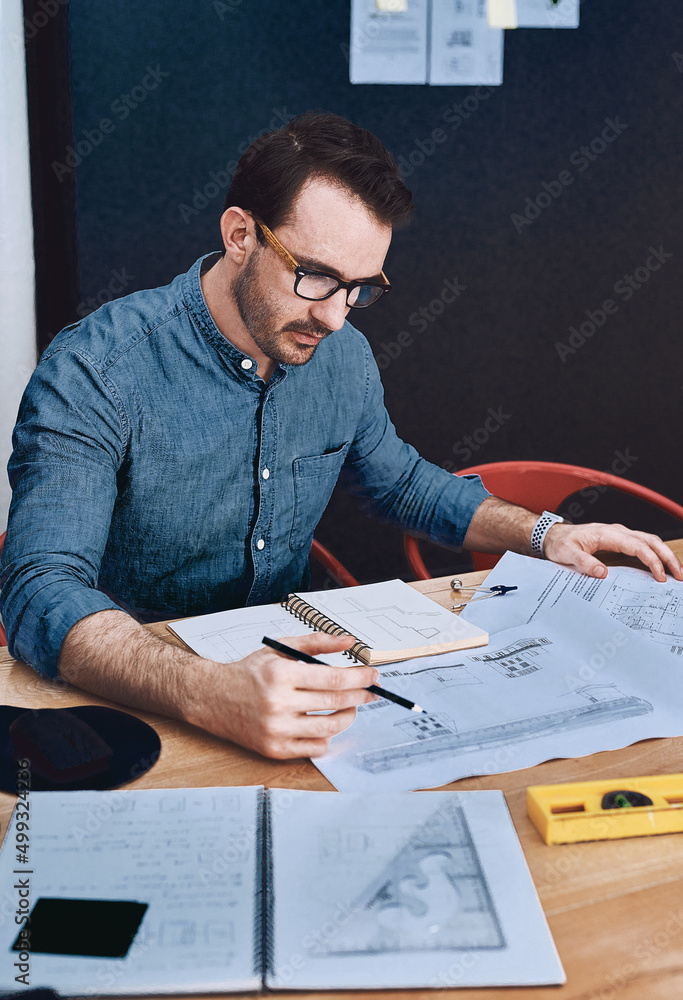 Poster creativity at work. cropped shot of a handsome young male architect working with blueprints in a mod