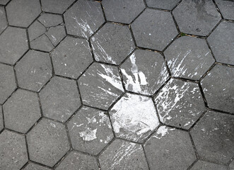 large splash of white paint fallen to the ground in the street, staining the gray hexagonal tiles