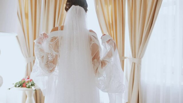 Morning of bride. Girl goes to window and sexually throws off transparent robe with lace from shoulders. Woman in white lingerie and nightgown and with veil on head. At end of frame is artistic effect