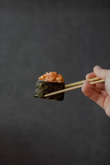 Roll with salmon close-up on a black background. Japanese kitchen. Fresh traditional delicious sushi. Sushi in hand close up. Restaurant menu