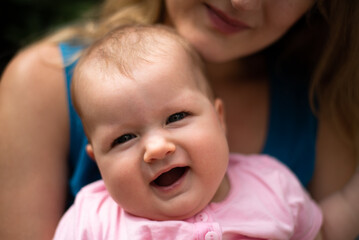 happy baby girl is smiling, mother holds child and looks on her - obrazy, fototapety, plakaty