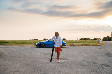 A young handsome man with long hair stands with a tripod somewhere on a country road, the...