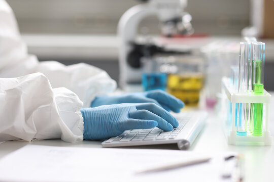 Hands of scientist in gloves works on keyboard in laboratory closeup