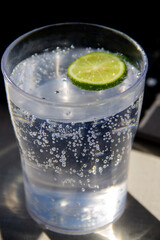a glass with a clear drink with bubbles and lime