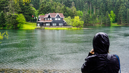 Woman photographer taking photo of impressive lake house. House on the shore of Cennet Gol...