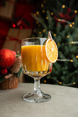 Shiny glass of hot orange grog cocktail served on counter in cafe on new year decoration background