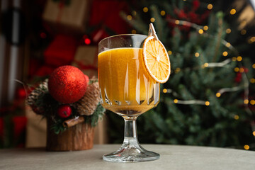 Shiny glass of hot orange grog cocktail served on counter in cafe on new year decoration background - obrazy, fototapety, plakaty