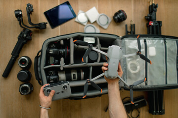 Professional  photographer packs smart backpack with equipment holding drone and remote control. Social media influencer top view on suitcase with lens, videocamera and camera, amateur drone and gimba
