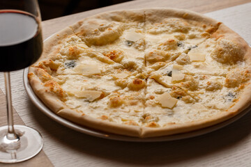 Four cheese pizza quattro formaggi with glass of wine on dark background.