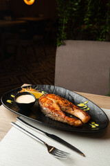 One piece of baked salmon steak grilled lemon and salt on a dark plate with white sauce