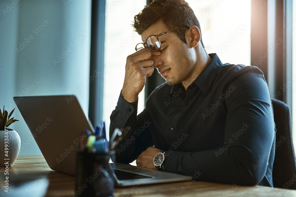 Wall mural When the stress of work triggers severe migraines. Shot of a young businessman looking stressed out while working on a laptop in an office.