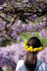 Giovane donna di spalle con corona di fiori nel giardino con glicine