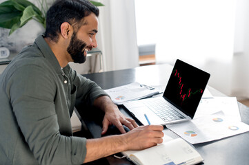 Smart concentrated indian successful broker investor, uses laptop to analyze financial...