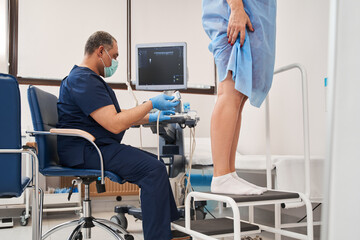 Caucasian young woman standing at the chair while having ultrasound on the legs