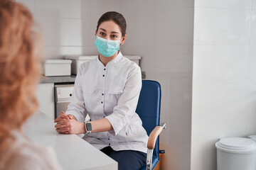 Fototapeta na wymiar Female doctor wearing protective mask working in the office and listening to the patient
