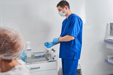 Obraz premium Serious caucasian doctor taking on protective gloves and preparing for the procedure at the clinic