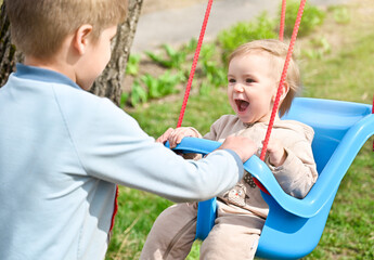 Brother rides little sister on a swing. The girl laughs merrily while riding on a swing.