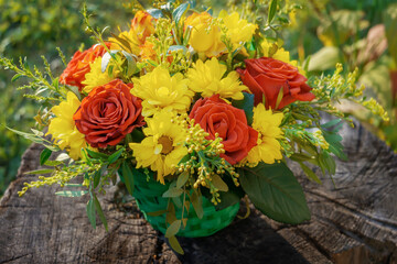 bouquet of flowers is a composition of red roses and chrysanthemums lying on a wooden stump on a green grass background. The background for the postcard