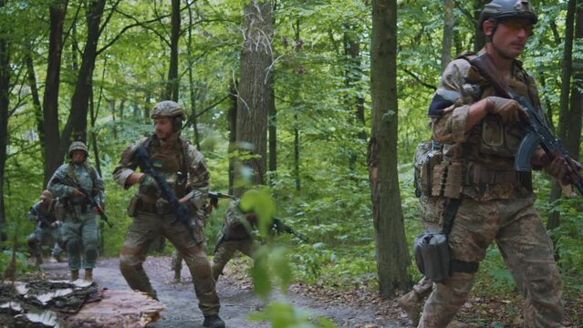 Group of soldiers in full gear a rifle in his hands in dense forest. All run away one soldier falls to the ground. War. Military concept