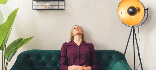 Panoramic shot of pensive young caucasian business blond-haired woman sitting on green sofa in waiting room. High quality photo
