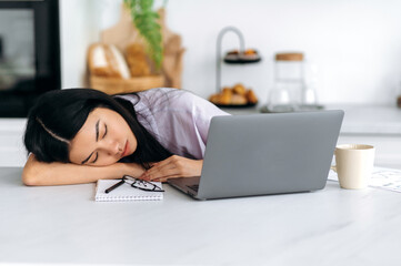 Obraz premium Fatigue concept. Tired exhausted Asian millennial girl, student or freelancer, fell asleep on the table while working remotely or studying in a laptop at home, is overworked, needs rest