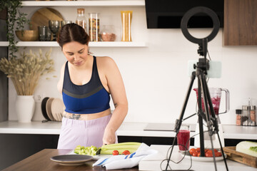 Woman with amputee arm chopping celery and recording video blog about healthy lifestyle