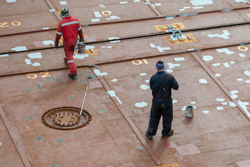 Seaman ship crew priming and derusting vessel deck for upcoming painting.
