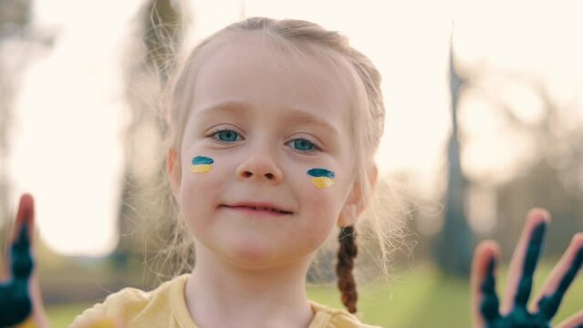 Close up portrait smiling little baby with flag of Ukraine on face and palms.