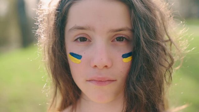 Close up portrait of serious girl with flag of Ukraine on face. Concept is no war in Ukraine.