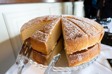 A Victoria Sponge cake cut into slices on a cake stand.