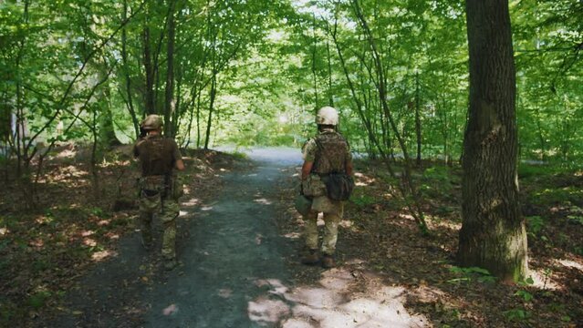 Shot back soldiers with fully equipped holds rifle wearing camouflage uniform walking in dense forest. Military concept. War