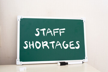 Staff Shortages. Chalk board with white pieces of chalk on a wooden table.