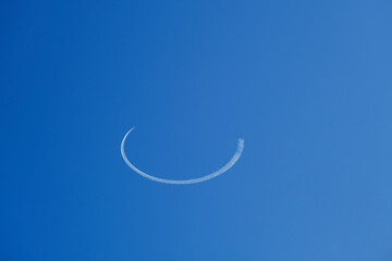 An airplane performing acrobatic flight in the blue sky. Trace of Smoke Behind. 
A trail of jet plane on blue sky.