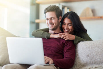 What you working on. Shot of an affectionate young couple using their laptop while relaxing on the...