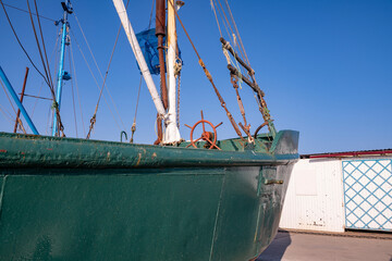 Green boat with red steering wheel and white mastrybatskaya green boat on the seafront.