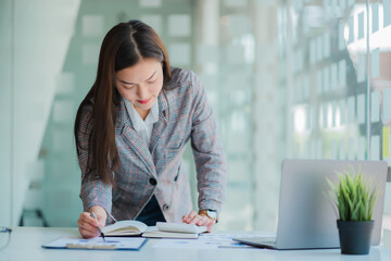 Asian businesswoman working on laptop computer and graph document calculator in the modern office is planning financial report analysis. business plan investment successful