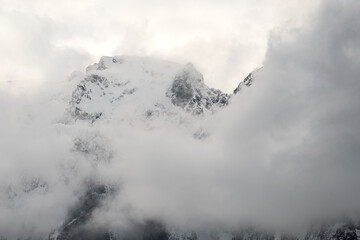 Clouds and fog shroud snow covered mountains and the mountain forests