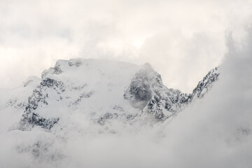 Clouds and fog shroud snow covered mountains and the mountain forests