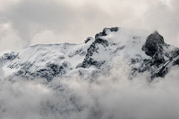 Clouds and fog shroud snow covered mountains and the mountain forests