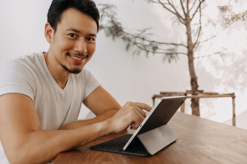 Happy freelance Asian man working with his tablet in the cafe.