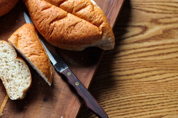 Bread is being sliced on a wooden cutting board. It's a freshly made bread. Photo Flat-lat