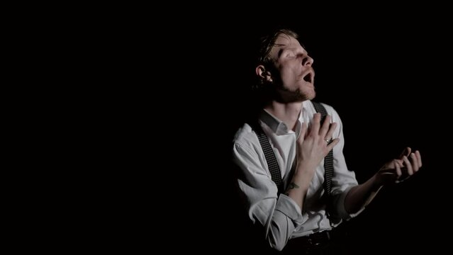 Handsome Man Artist in theatre or a musician emotionally shows a performance, sing and dancing in the dark room isolated on black.