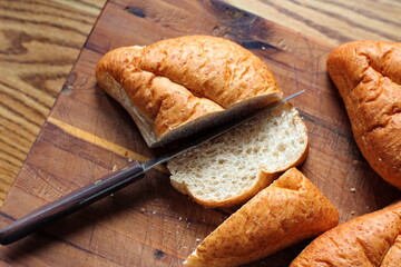 wheat bolillos made from wheat being sliced and ready to serve On a wooden cutting board at the kitchen table. Flat-lat photo.