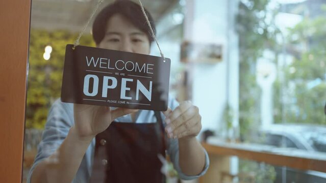 Business owner asian man turning Welcome we are open sign on fronton glass door store.